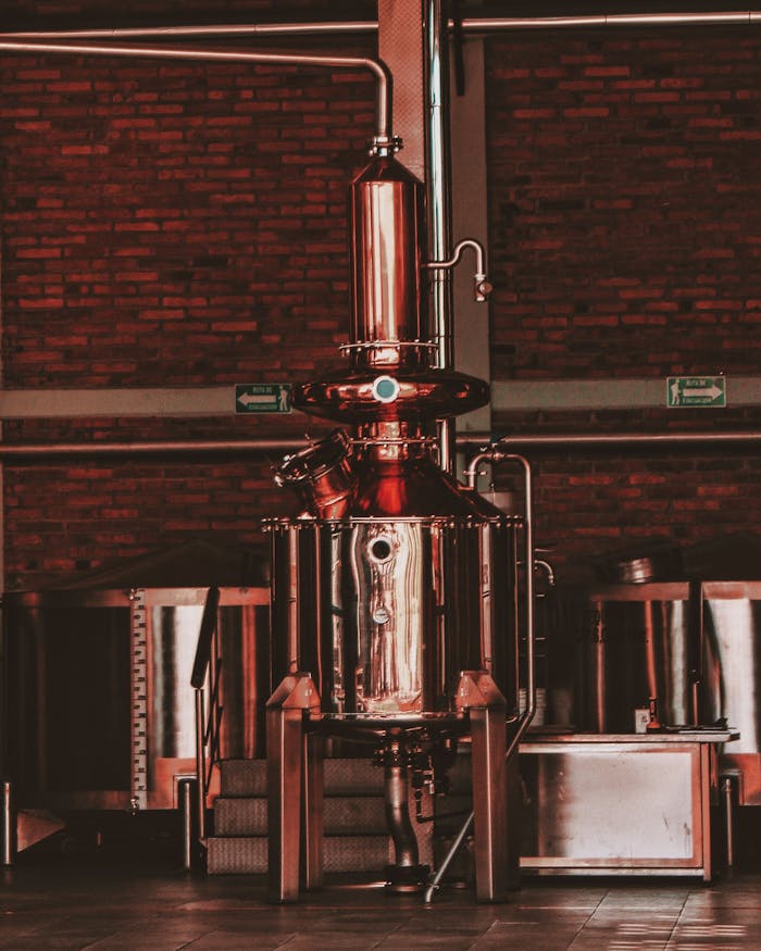 Close-up of stainless steel distillery equipment in an industrial setting, featuring pipes and machinery.