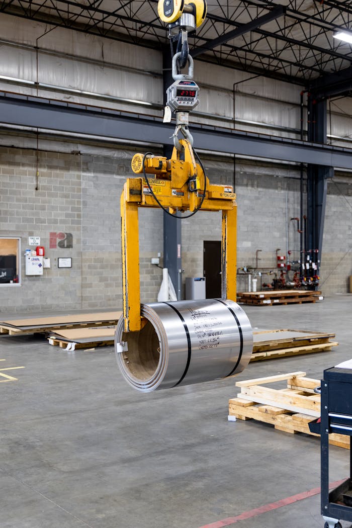 Metal coil being lifted by a crane inside an industrial manufacturing facility.